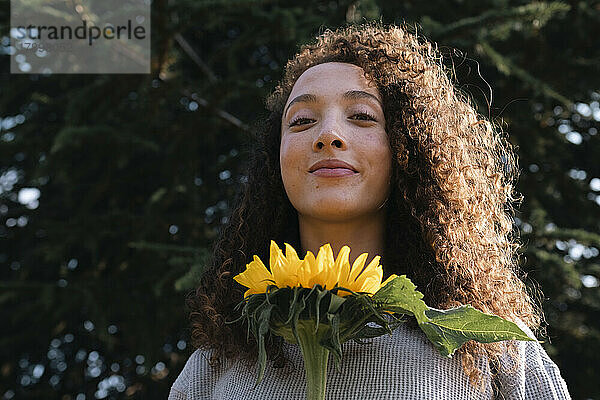 Lächelnde junge Frau mit Sonnenblume an einem sonnigen Tag