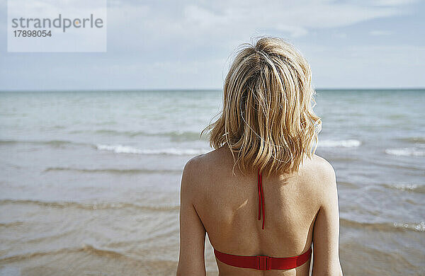Frau mit blonden Haaren blickt aufs Meer