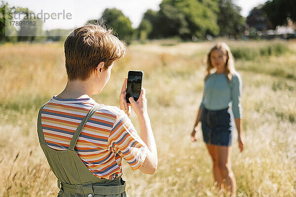 Nicht-binäre Person fotografiert an einem sonnigen Tag einen Freund per Smartphone
