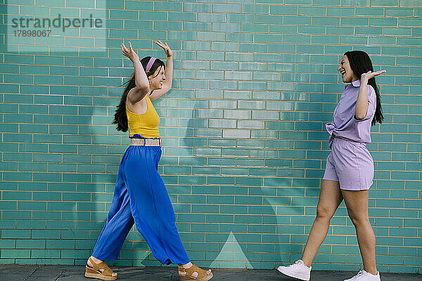 Carefree friends walking towards each other in front of turquoise brick wall