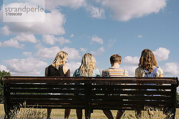 Freunde sitzen zusammen auf einer Parkbank unter bewölktem Himmel