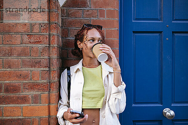Junge Frau trinkt Kaffee aus Einwegbecher vor der Wand
