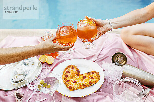 Hände von Frauen  die am Tisch am Pool Cocktails anstoßen