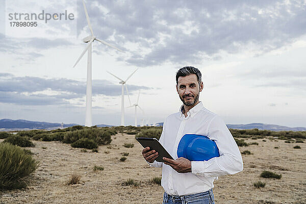 Selbstbewusster Ingenieur mit Helm und Tablet-PC im Windpark