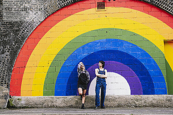 Freunde stehen zusammen vor einem an die Wand gemalten Regenbogen