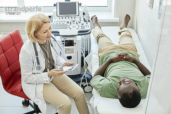 Doctor explaining ultrasound to patient lying on bed in clinic