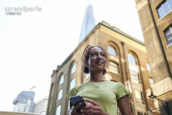 Lächelnde junge Frau mit Mobiltelefon vor dem Gebäude