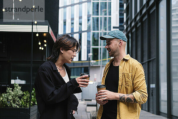 Schwules Paar mit Kaffeetassen redet vor Gebäuden