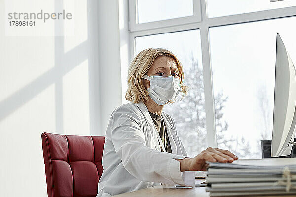 Arzt erledigt Papierkram und trägt eine schützende Gesichtsmaske in der Klinik