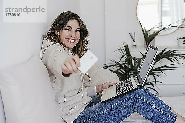 Glückliche junge Frau mit Laptop und Kreditkarte