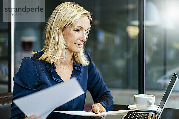 Lächelnde Geschäftsfrau mit Dokumenten  die auf den Laptop schaut