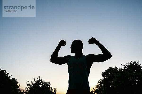 Silhouette eines jungen Mannes  der bei Sonnenuntergang seine Muskeln spielen lässt