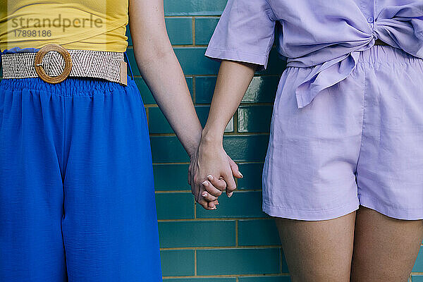 Young women holding hands standing in front of brick wall