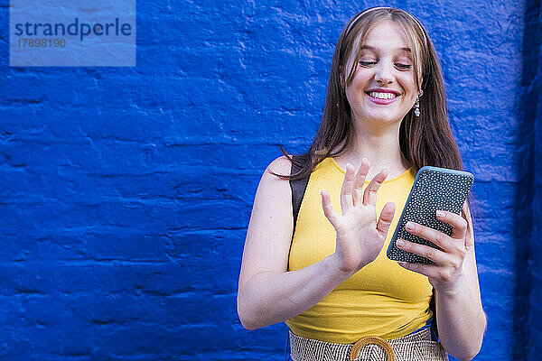 Lächelnde Frau benutzt Smartphone vor blauer Wand