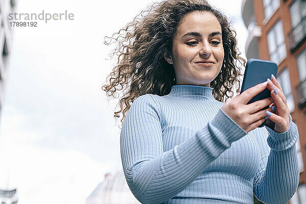 Lächelnde Frau mit lockigem Haar  die ihr Smartphone benutzt