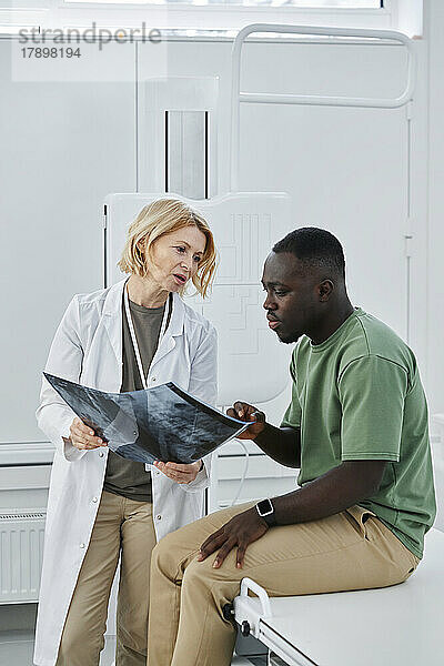 Arzt hält Röntgenbild im Gespräch mit Patient in der Klinik
