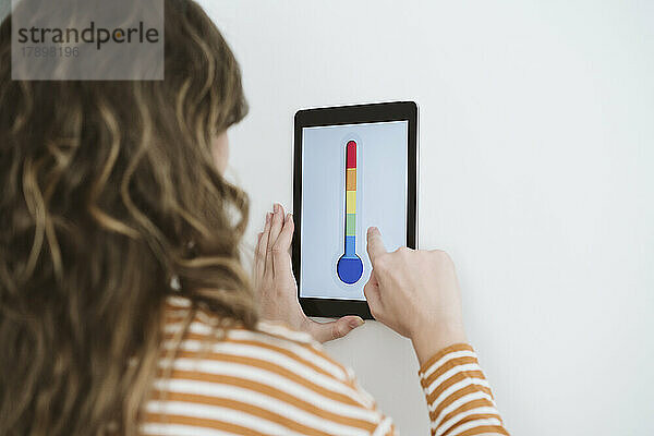 Junge Frau benutzt digitales Tablet mit Thermometersymbol an der Wand