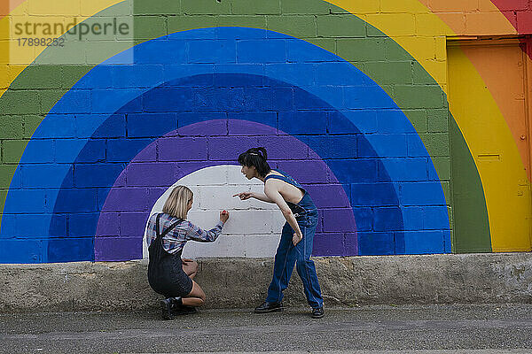 Frau mit Freundin schreibt auf Regenbogenwandbild