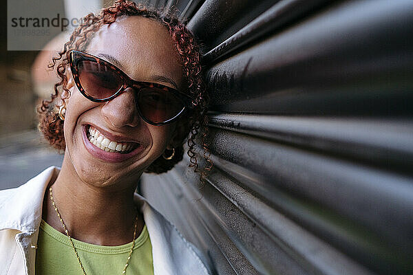 Happy young woman wearing sunglasses leaning on wall