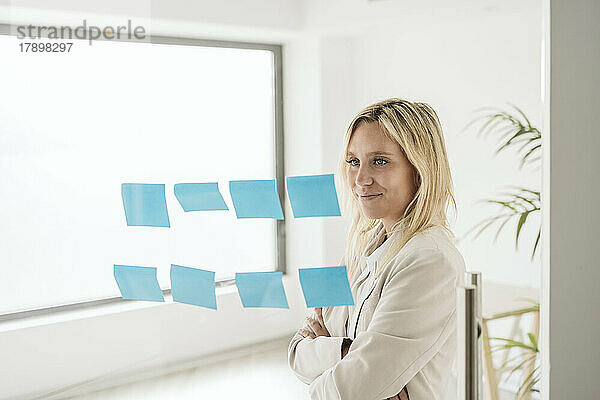 Businesswoman looking at adhesive notes on glass wall in office