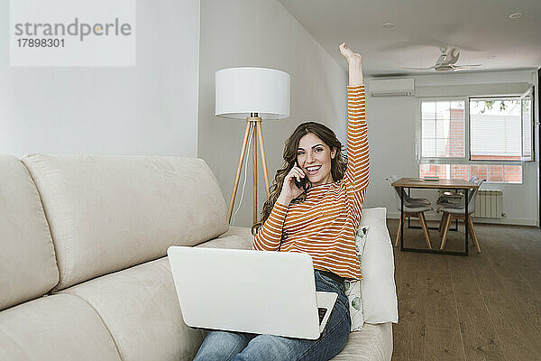 Glückliche junge Frau mit Laptop auf dem Sofa  die telefoniert