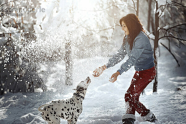 Verspielte Frau mit Dalmatiner im Schnee im Park