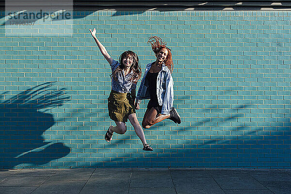 Fröhliche junge Freunde springen gemeinsam vor der Wand
