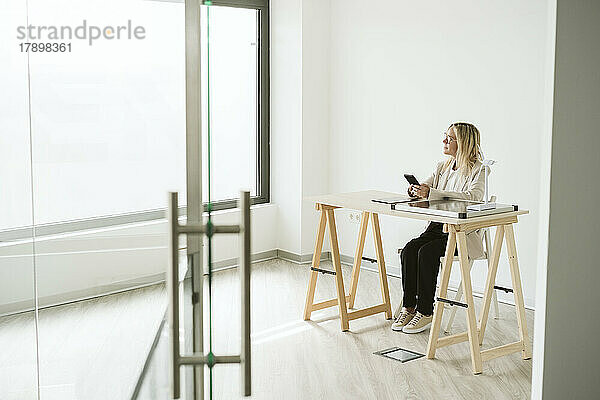 Frau sitzt am Schreibtisch im Büro mit Mobiltelefon und Solarpanel