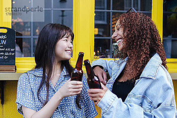 Fröhliche Freunde  die vor dem Fenster Bierflaschen anstoßen