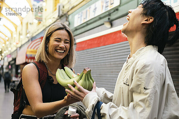 Glückliche junge Frau  die einem Freund auf der Straße Bananen schenkt