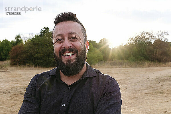 Glücklicher reifer Mann mit Bart im Feld bei Sonnenuntergang