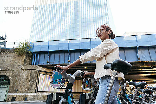 Lächelnde Frau mit Elektrofahrrad am Parkplatz