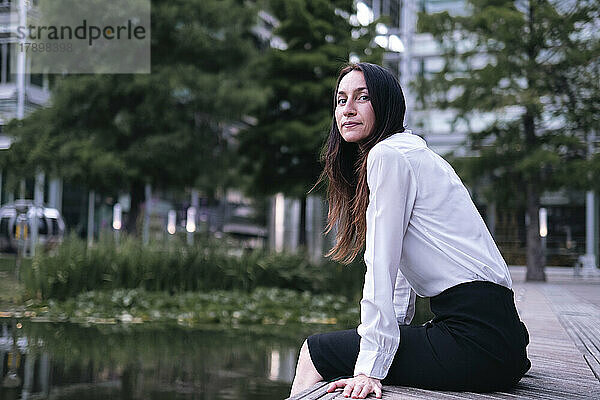 Reife Geschäftsfrau sitzt entspannt am See im Park