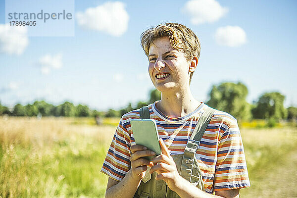 Lächelnde nicht-binäre Person mit Smartphone  die an einem sonnigen Tag im Park steht