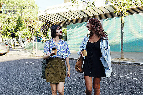 Fröhliche Freunde mit einer Kaffeetasse  die auf der Straße spazieren gehen