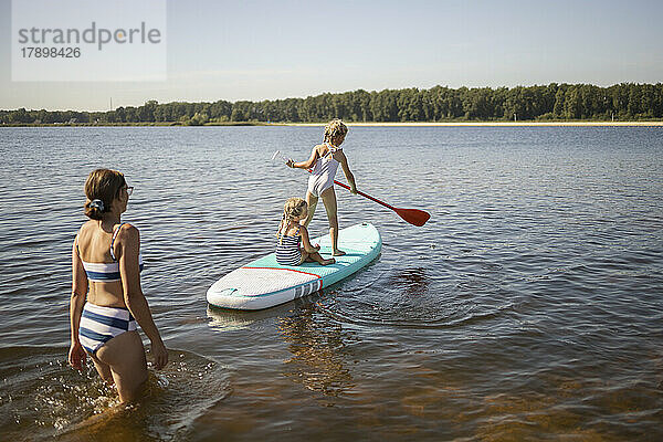 Mädchen vergnügen sich mit ihrer Mutter auf dem Paddleboard am See