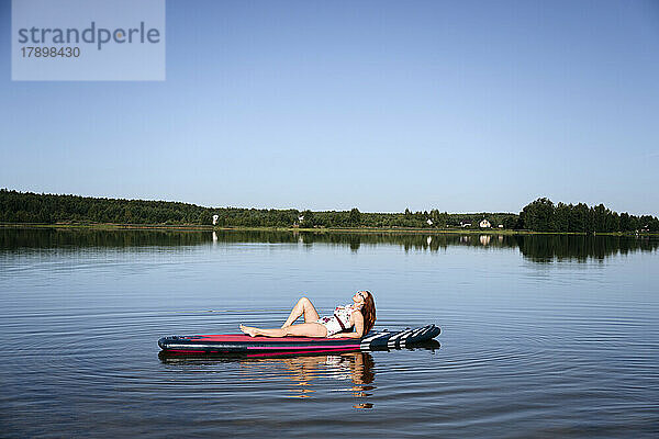 Woman relaxing on SUP board in lake under blue sky