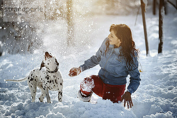 Verspielte Frau wirft im Park Schnee auf dalmatinischen Hund