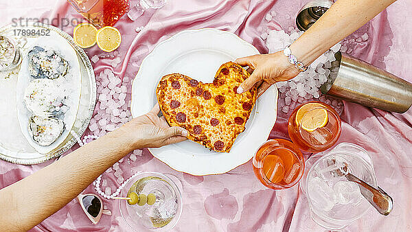 Hände von Frauen  die herzförmige Pizza am Tisch ziehen