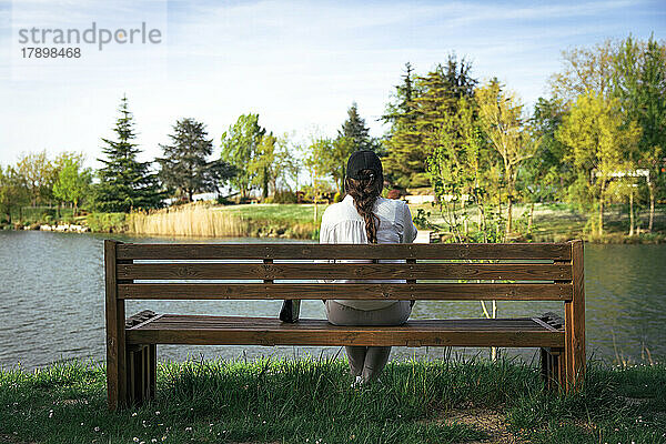 Junge Frau sitzt auf einer Bank vor dem See im Park