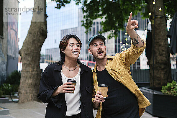Mann hält Kaffeetasse und Freund zeigt in die Stadt