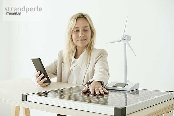 Frau benutzt Mobiltelefon mit Solarpanel und Windturbinenmodell auf dem Schreibtisch