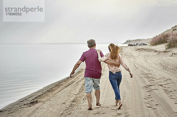 Vater und Tochter gehen bei Sonnenuntergang gemeinsam im Sand spazieren