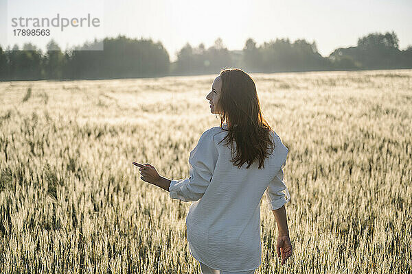 Frau zeigt  wie sie an einem sonnigen Tag im Maisfeld spaziert