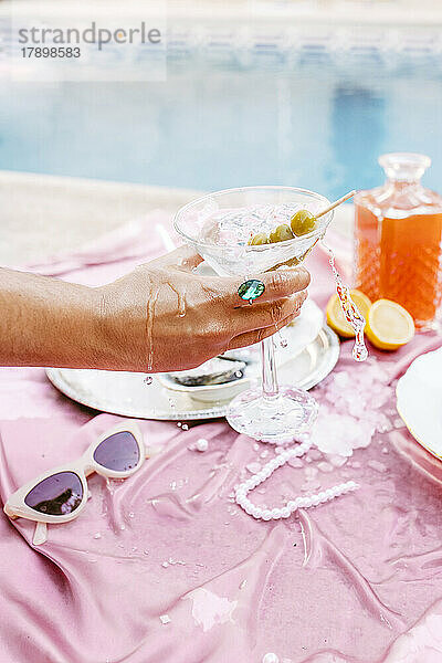 Hand einer Frau  die Martini-Glas am Tisch hält