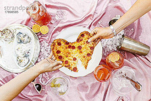 Freunde ziehen herzförmige Peperoni-Pizza am Tisch
