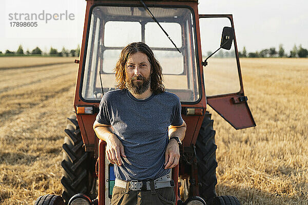 Reifer Mann stützt sich auf Traktor auf Bauernhof