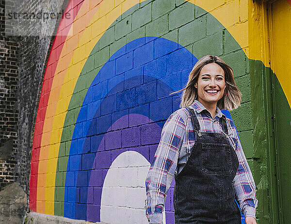 Glückliche junge Frau  die an einem Regenbogenwandbild an der Wand vorbeigeht