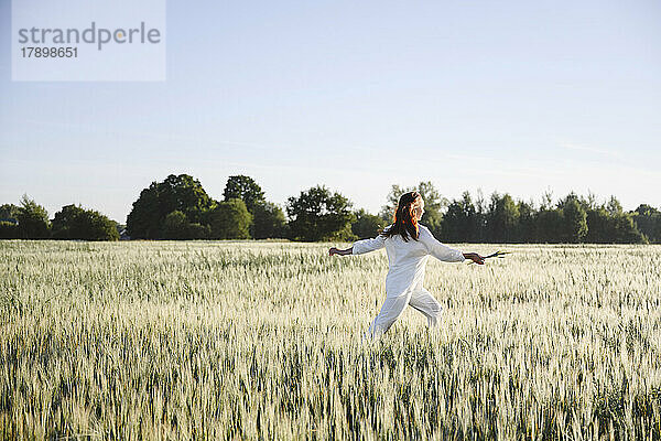 Unbeschwerte Frau läuft an einem sonnigen Tag im Maisfeld