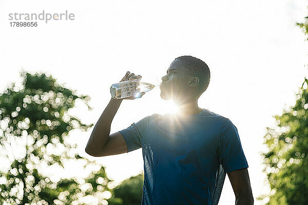Junger Mann trinkt an sonnigem Tag Wasser aus der Flasche